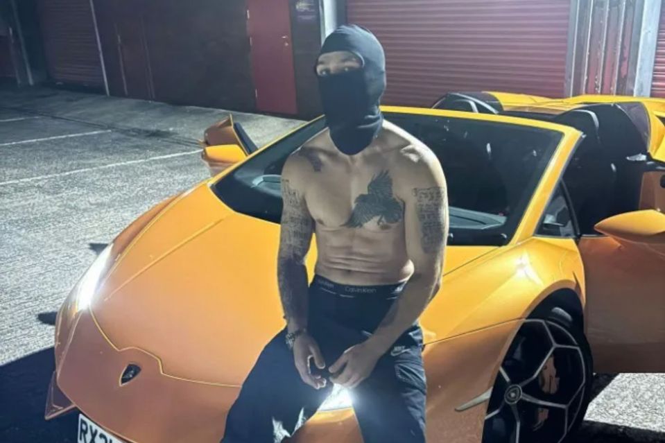 A shirtless man wearing a balaclava sits on a yellow Lamborghini.