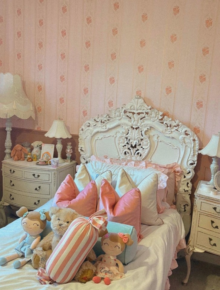 Girl's bedroom with ornate white bed, pink pillows, and dolls.