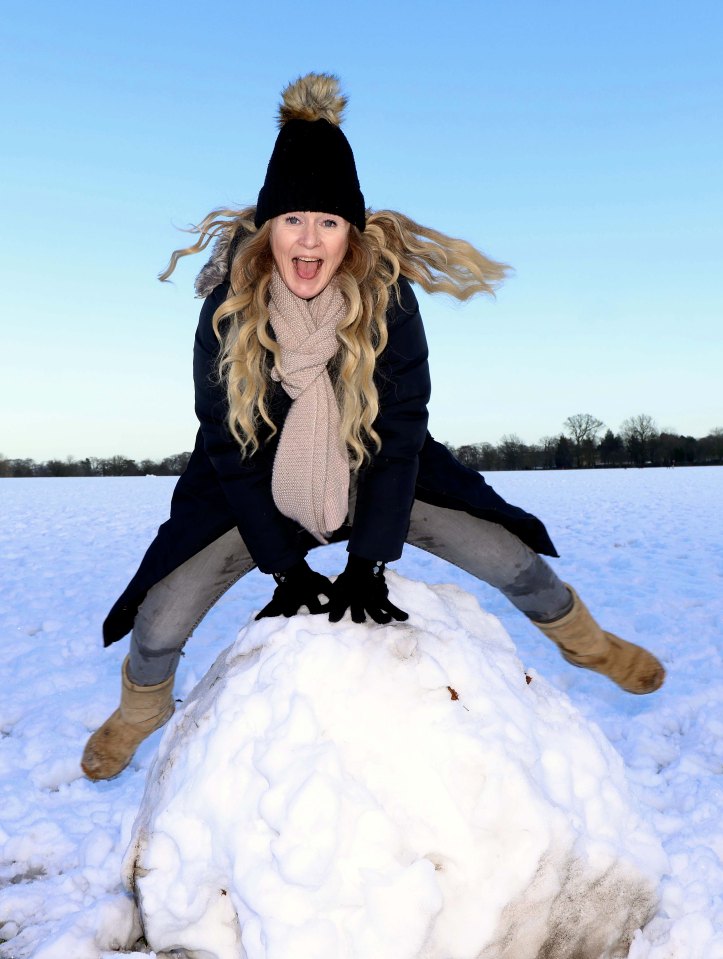 Woman leaping over a large snowball in a snowy field.