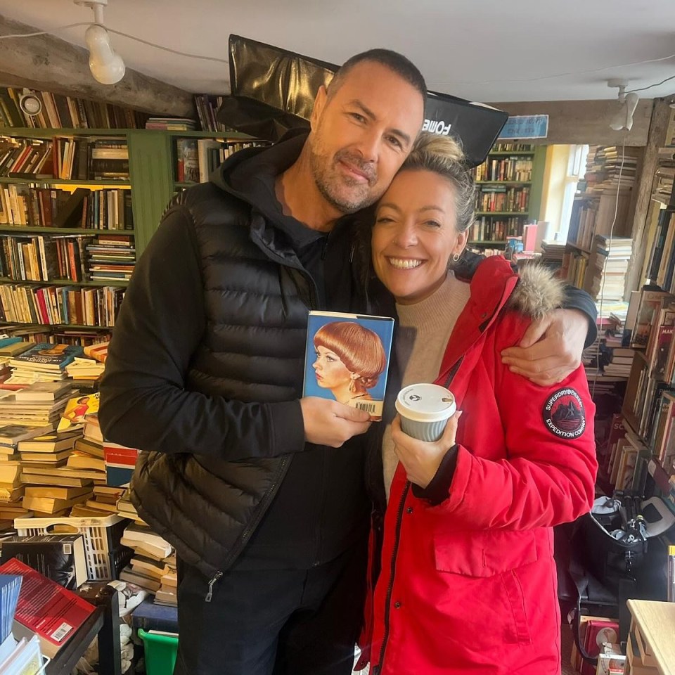 Paddy McGuinness and a woman holding a book and a coffee cup, surrounded by bookshelves.