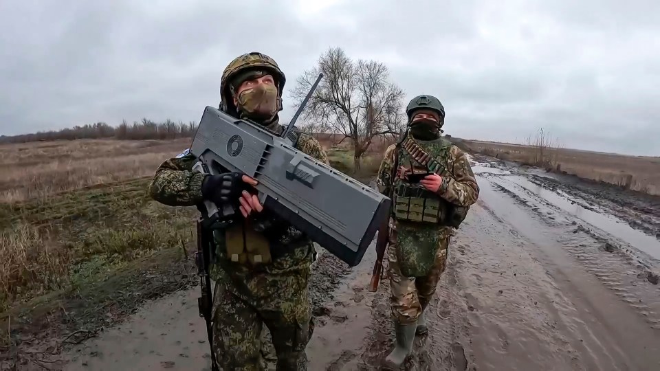 Two Russian soldiers carrying weapons walk along a muddy road.