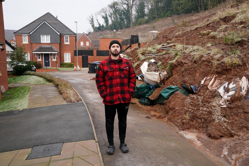 Man standing in front of a large landslide blocking a residential road.