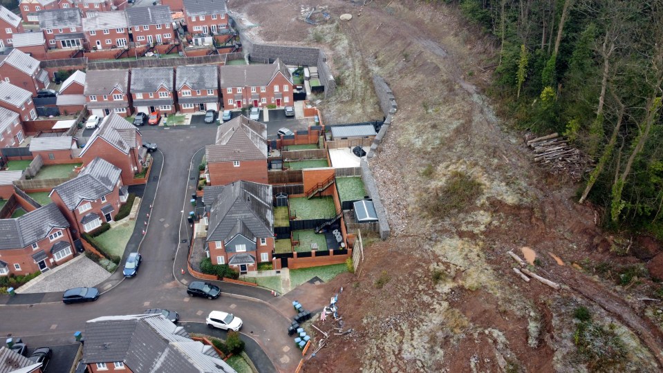 Aerial view of a massive landslip blocking a road and isolating homes.