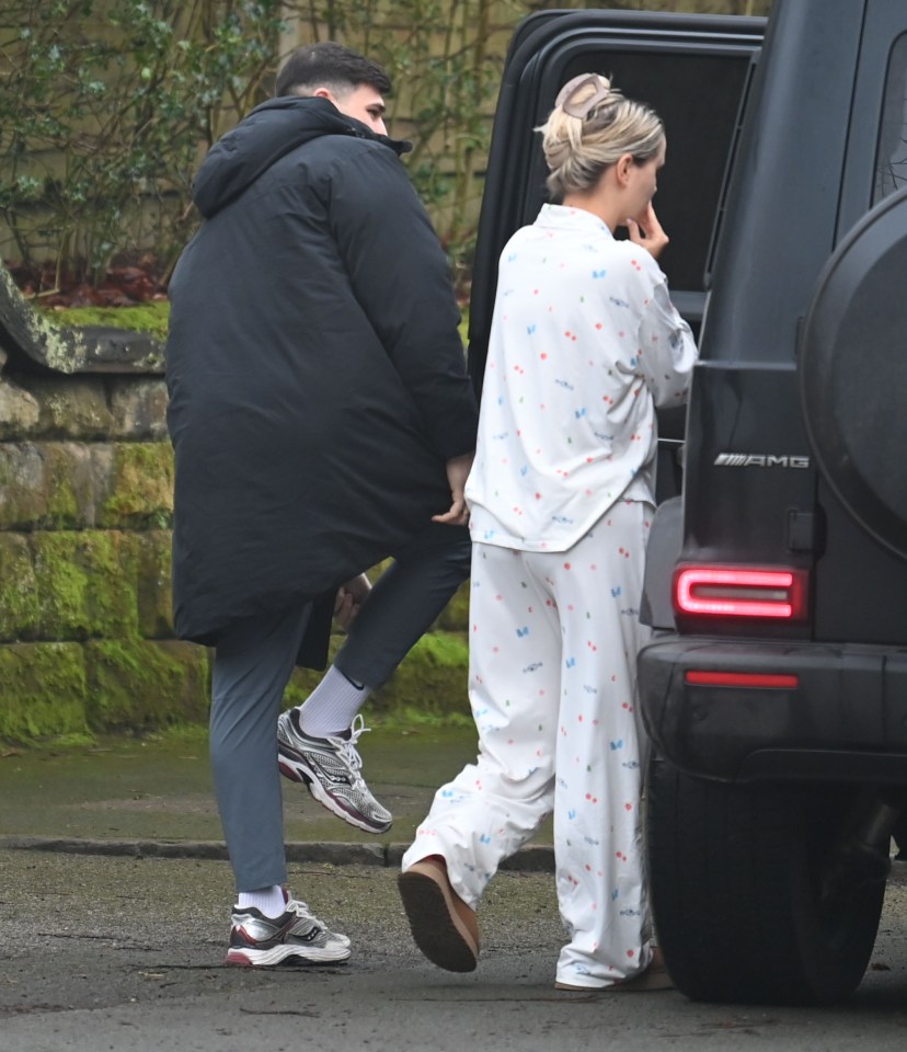 A woman in pajamas and a man in a long coat walk toward a car.