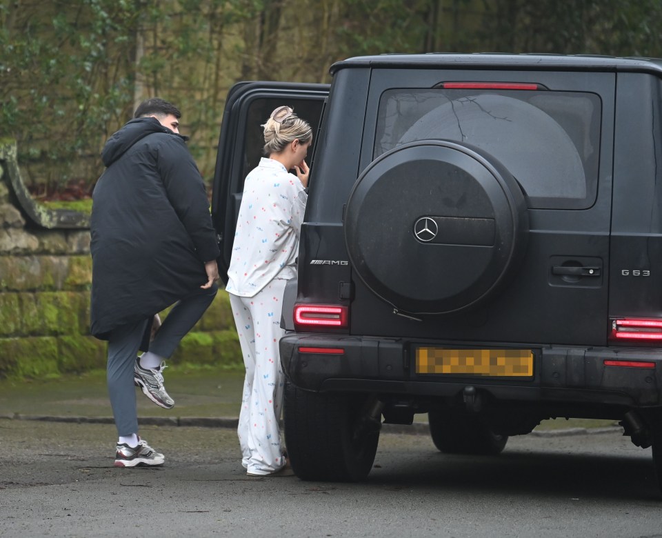 A woman in pajamas gets into a black Mercedes G-Class SUV as a man watches.