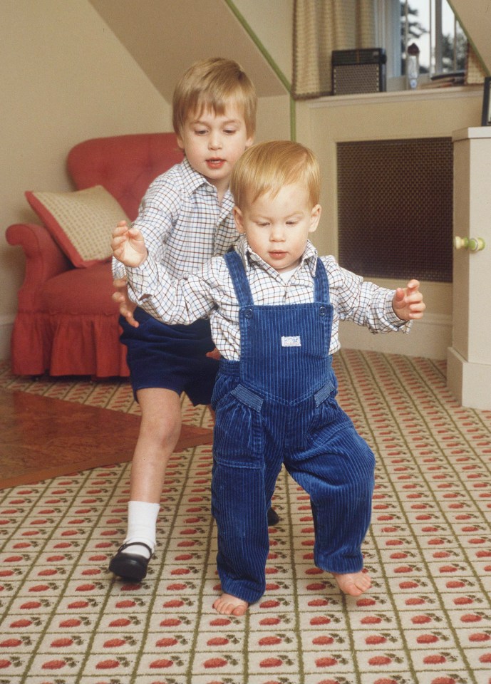 Prince William assisting Prince Harry with his first steps in their Kensington Palace playroom.