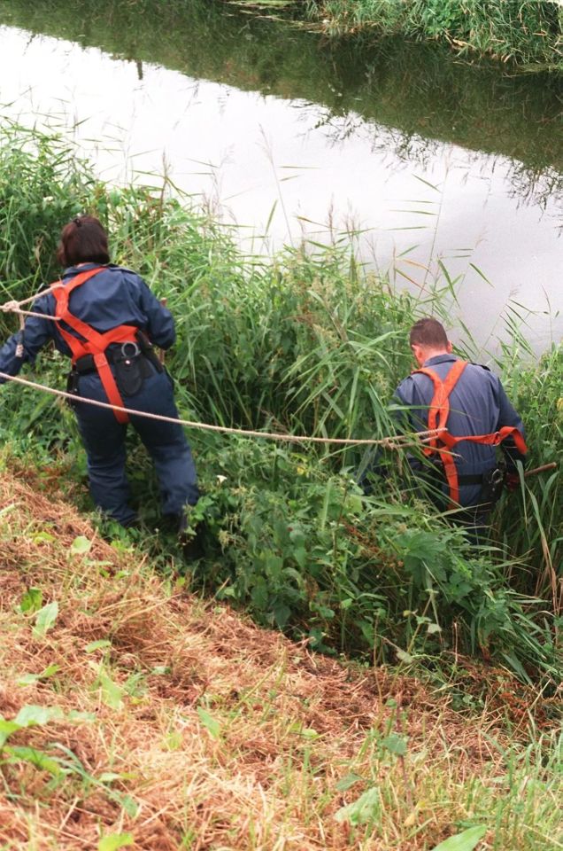 Police officers searching a drain.