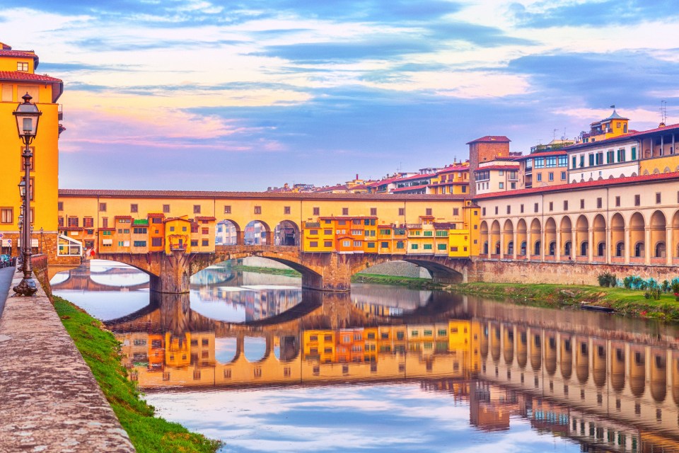 Ponte Vecchio in Florence, Italy, reflecting in the Arno River at sunset.