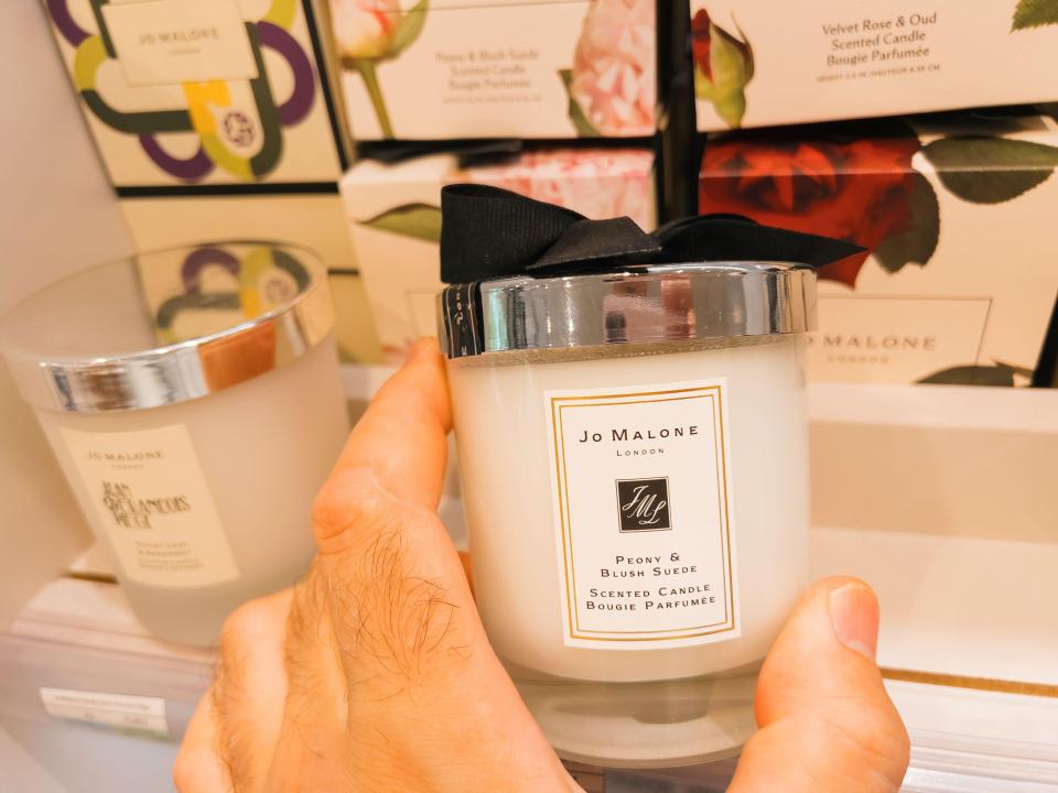 A hand holding a Jo Malone Peony & Blush Suede scented candle.