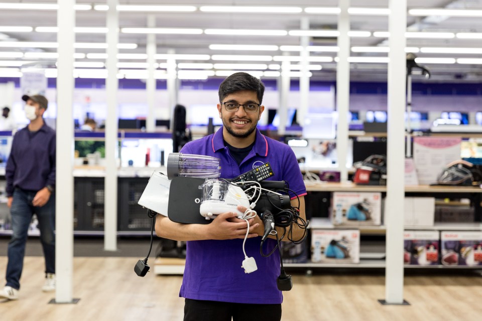 A Currys employee holding a pile of electronics.