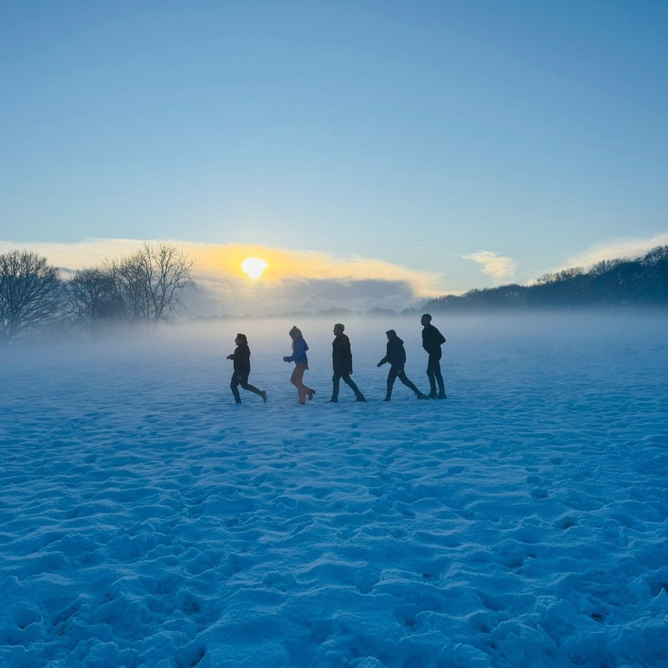 Five people walking in a snowy field at sunset.