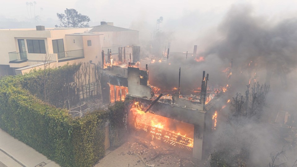 A house engulfed in flames during a wildfire.