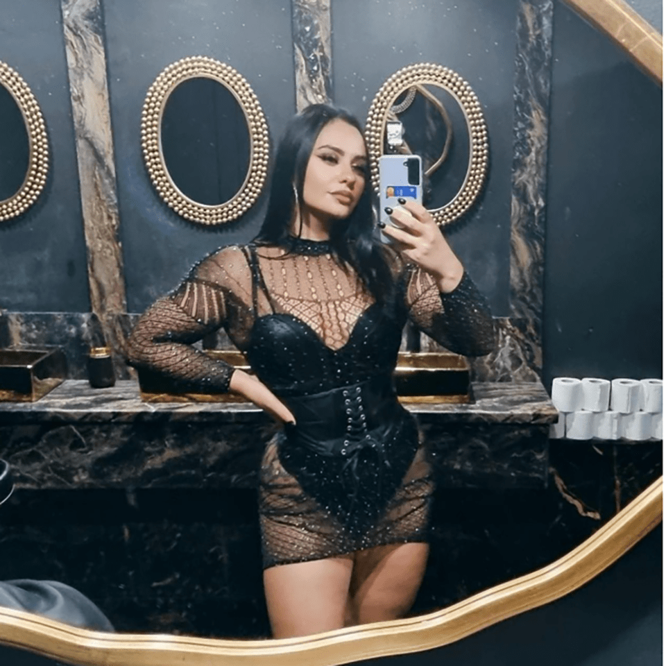 Woman in a black, sequined mini-dress taking a selfie in a restroom.