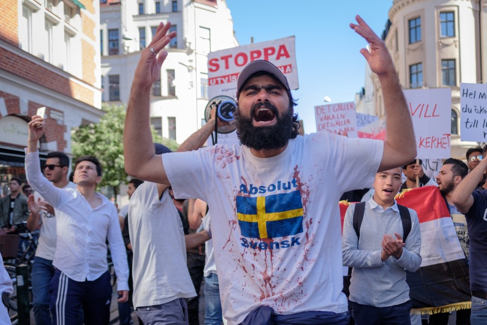 A protester shouts slogans at a demonstration against migrant deportations, wearing a t-shirt stained with fake blood.