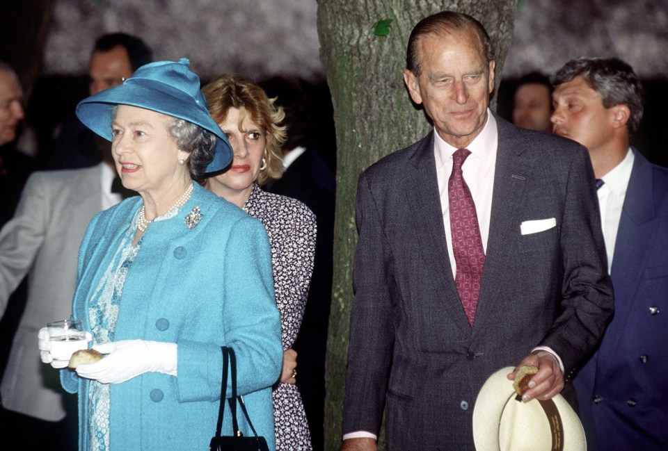 The Queen and Prince Philip during a visit, holding a bread roll and a glass of water.