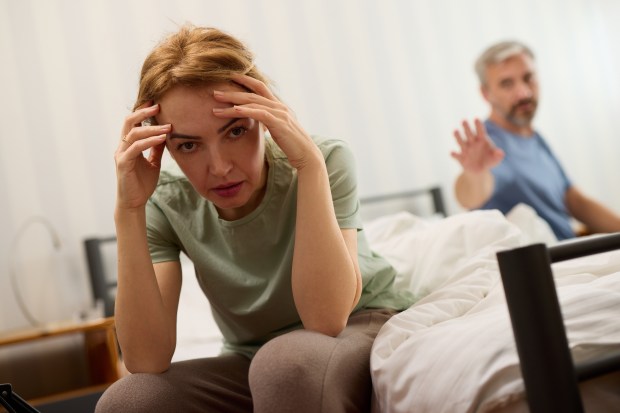 Upset woman sitting on bed, man in background.