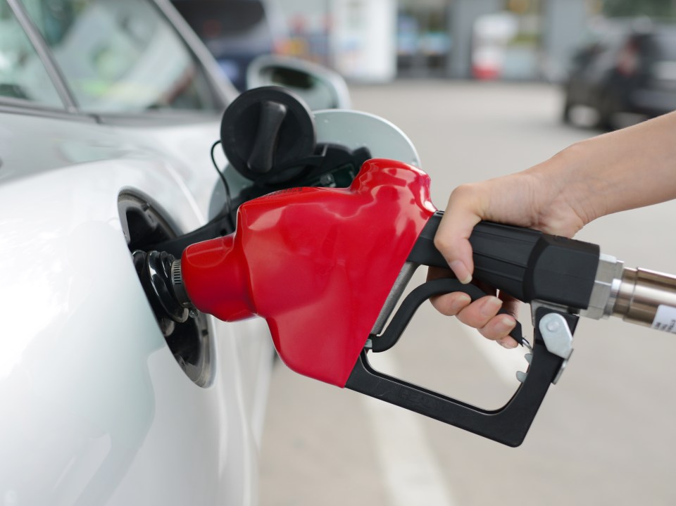 A hand holding a gas pump nozzle inserting it into a car's fuel tank.