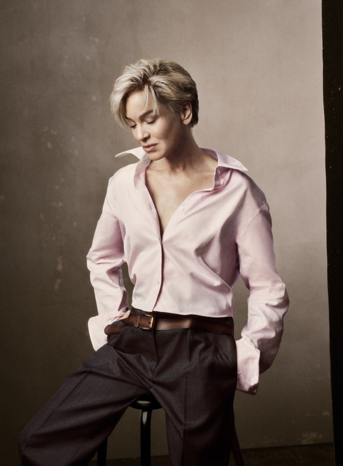 Renée Zellweger in a pink shirt and dark trousers.