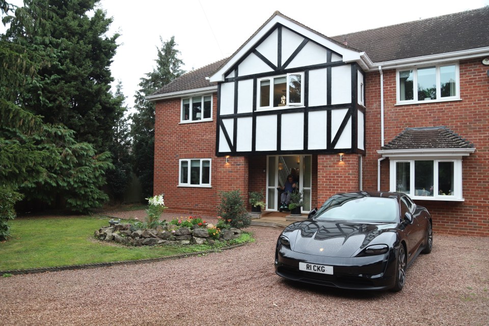 Black Porsche Taycan parked in front of a large brick house.