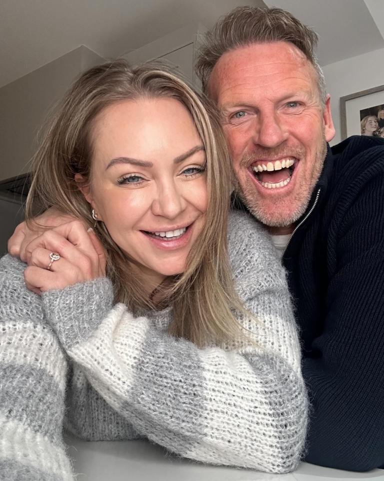 Couple smiling for a photo.  The woman is wearing a grey and white sweater.