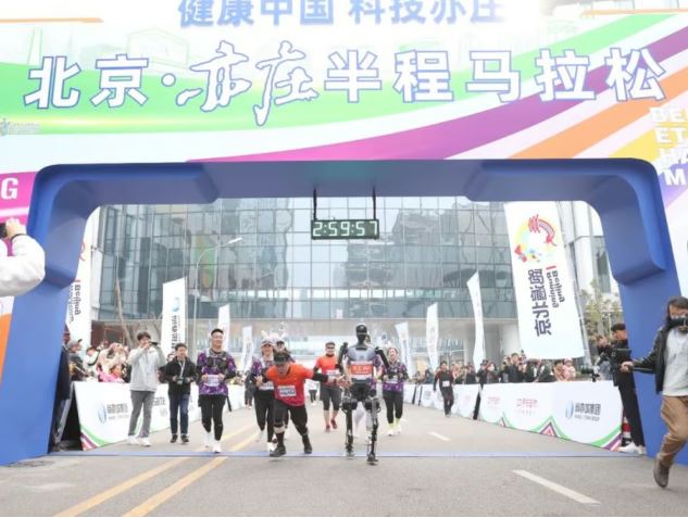 Robot and human runners crossing a half-marathon finish line.