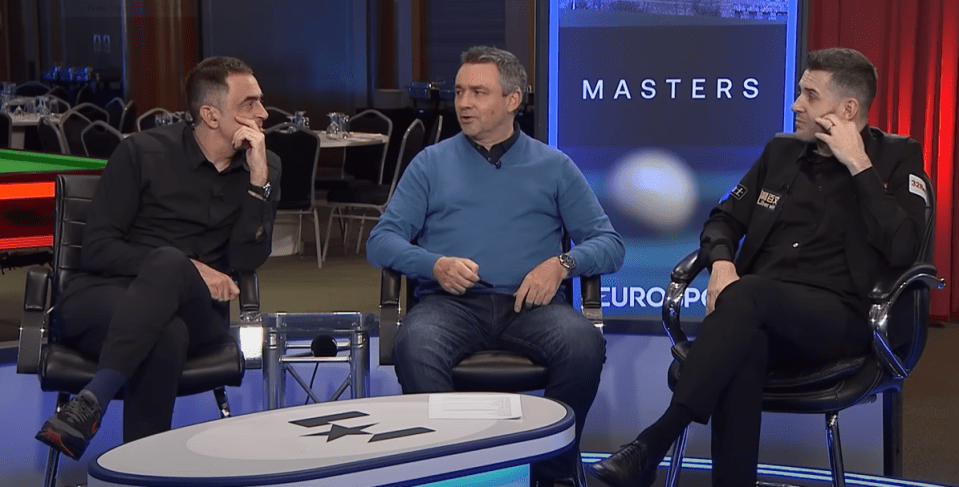 Three men sitting on chairs and talking during a snooker tournament.