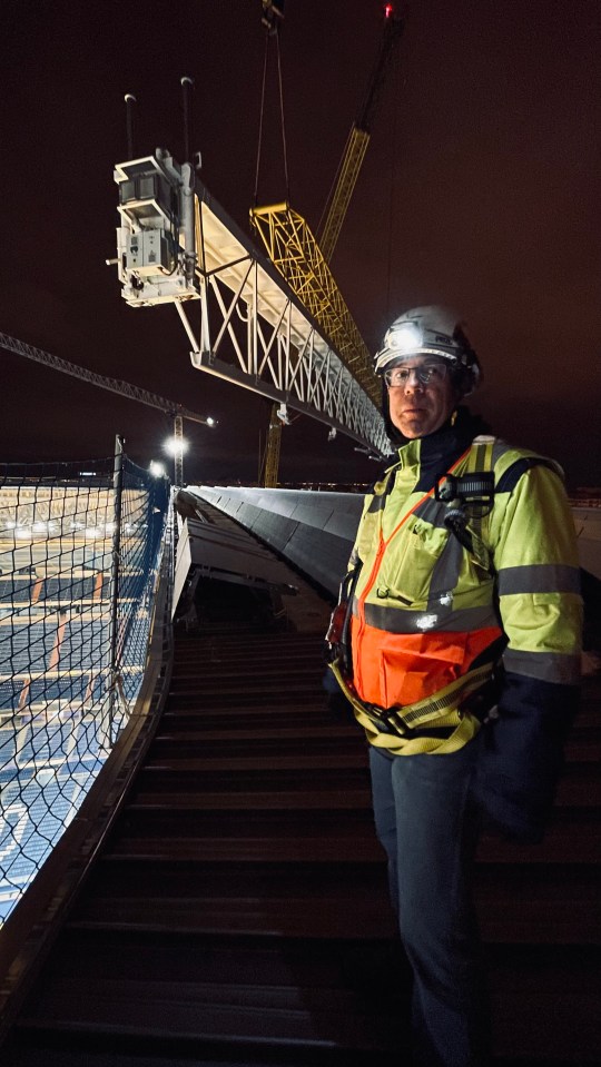 Construction manager overseeing the installation of a retractable roof section at night.