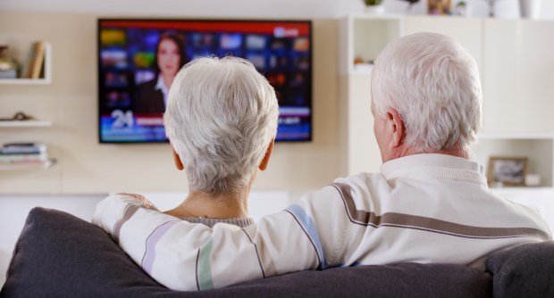 Senior couple sitting on a sofa watching television.