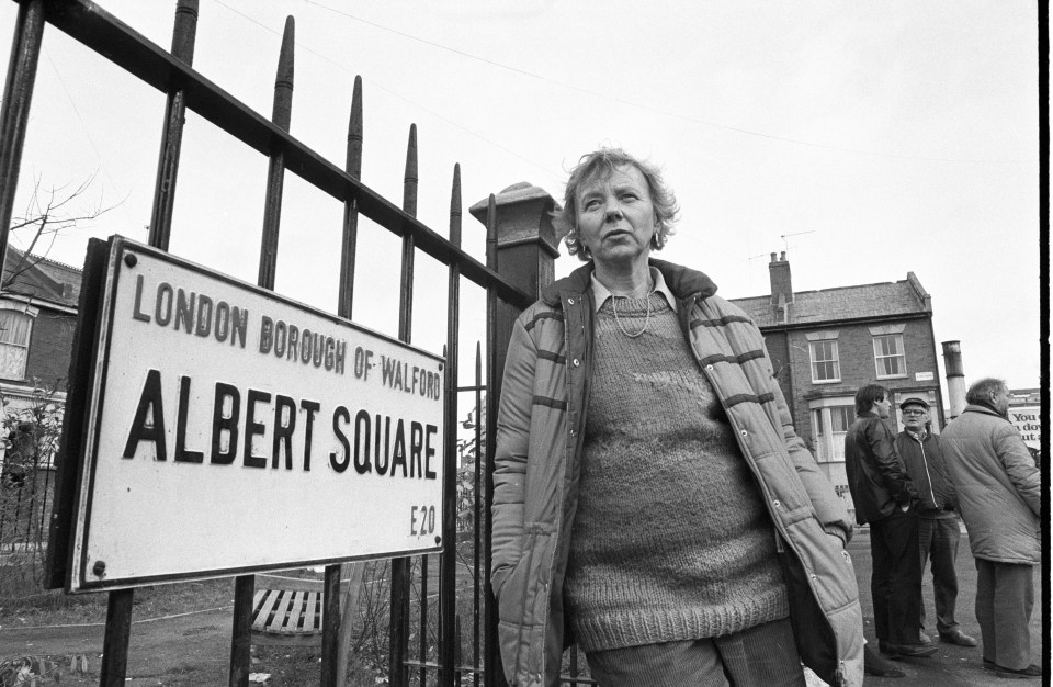 Black and white photo of Julia Smith, producer of the BBC soap Eastenders, standing by an Albert Square street sign.