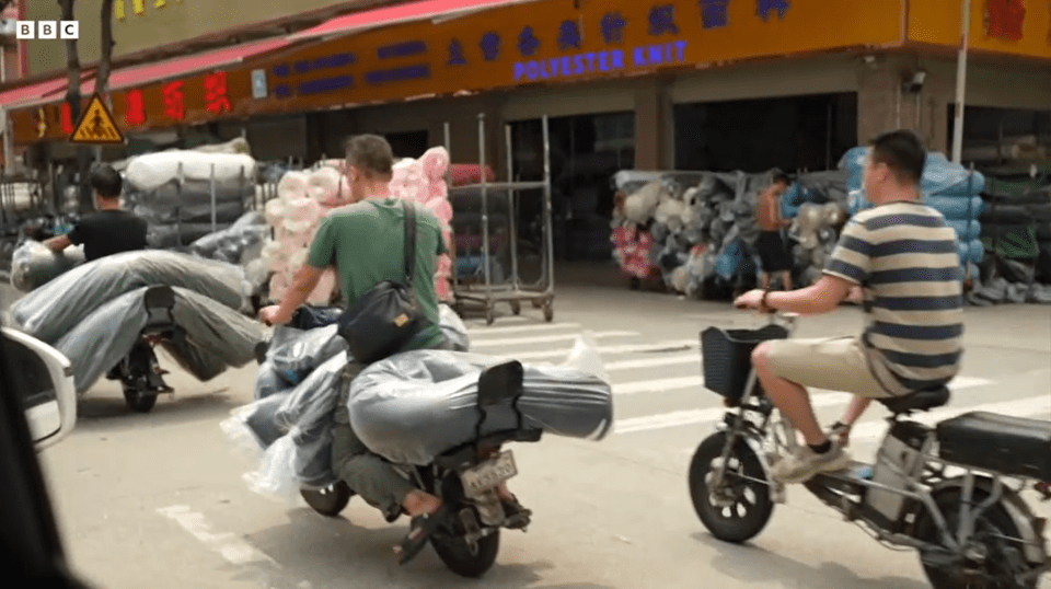 People on motorcycles and scooters carrying large bundles of fabric outside a polyester knit factory.