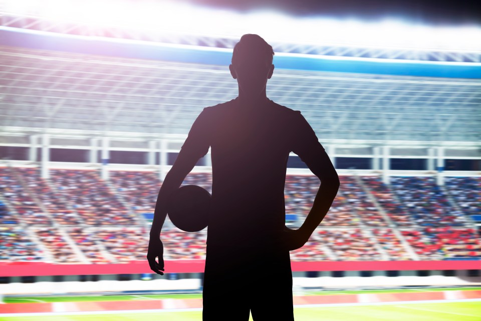 Silhouette of a soccer player holding a ball in a stadium.