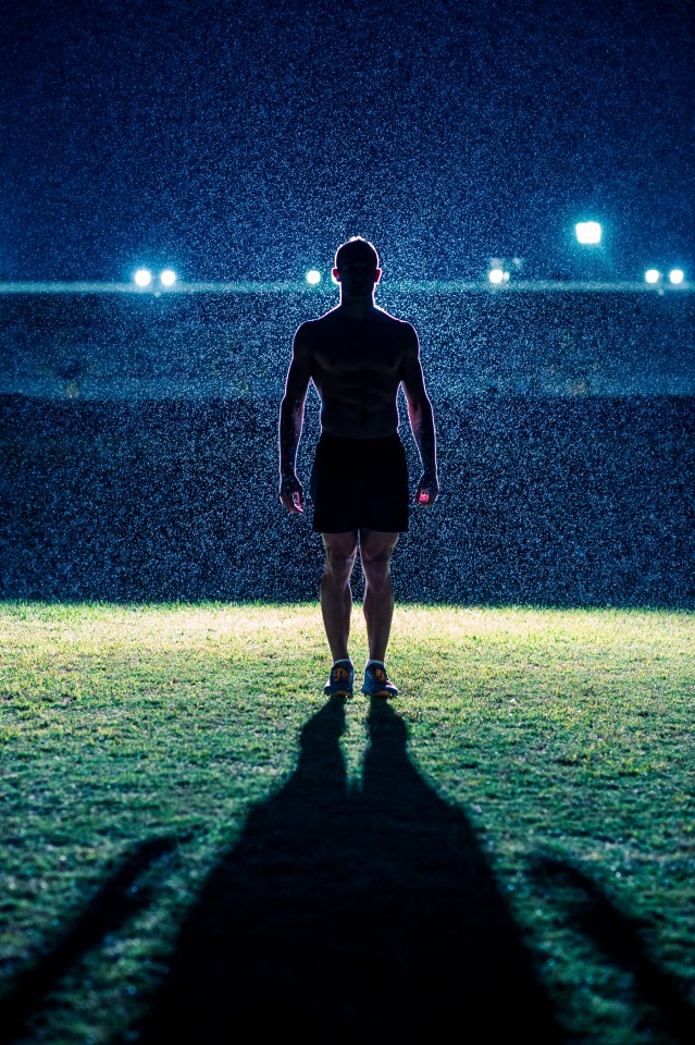 Silhouette of a muscular man standing in the rain at night.