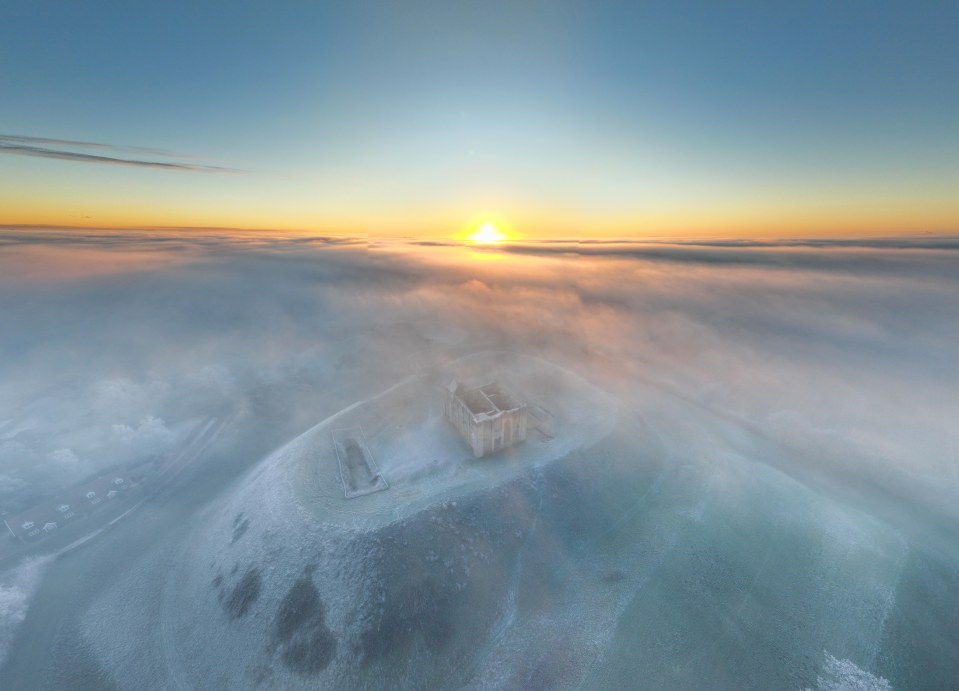 Aerial view of Castle Rising at sunrise, covered in freezing fog.