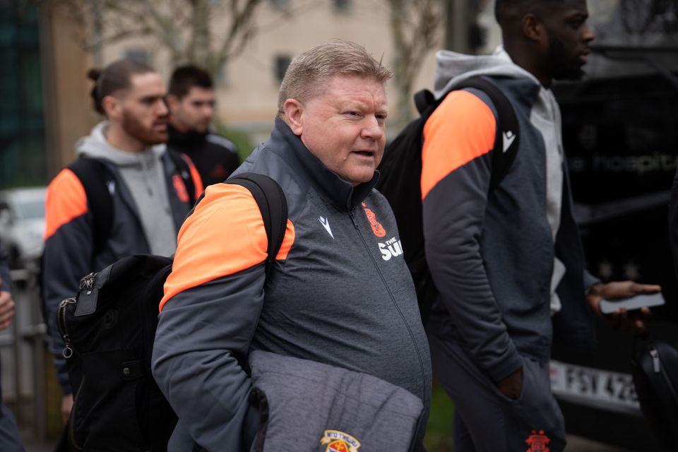 A man in a gray and orange jacket walks with a backpack, other people in similar jackets are blurred in the background.