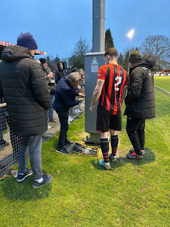 A footballer, who is also an electrician, repairs a broken floodlight at a football stadium.