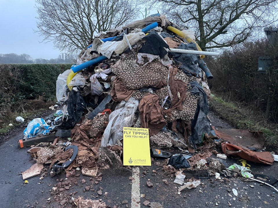 Large pile of fly-tipped waste blocking a road, with a witness appeal sign.