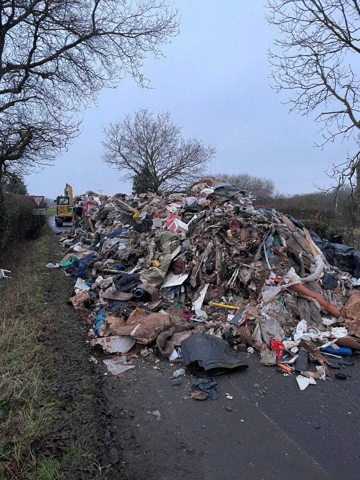 A large pile of fly-tipped building waste blocking a road.