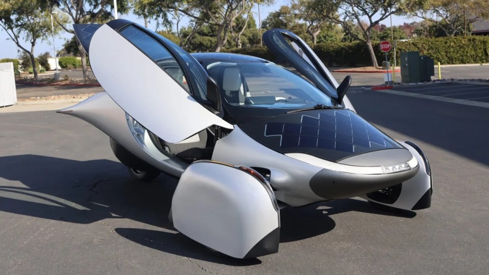 Three-wheeled solar-powered car with gull-wing doors open.