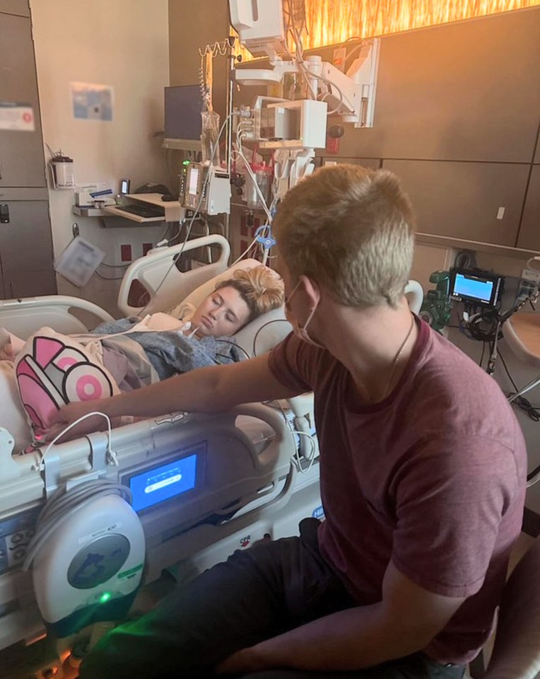 A young woman in a hospital bed, with a man sitting beside her.