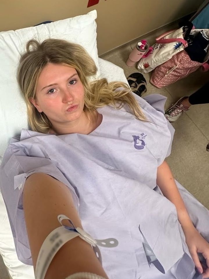 A young woman in a hospital gown lies in a hospital bed.