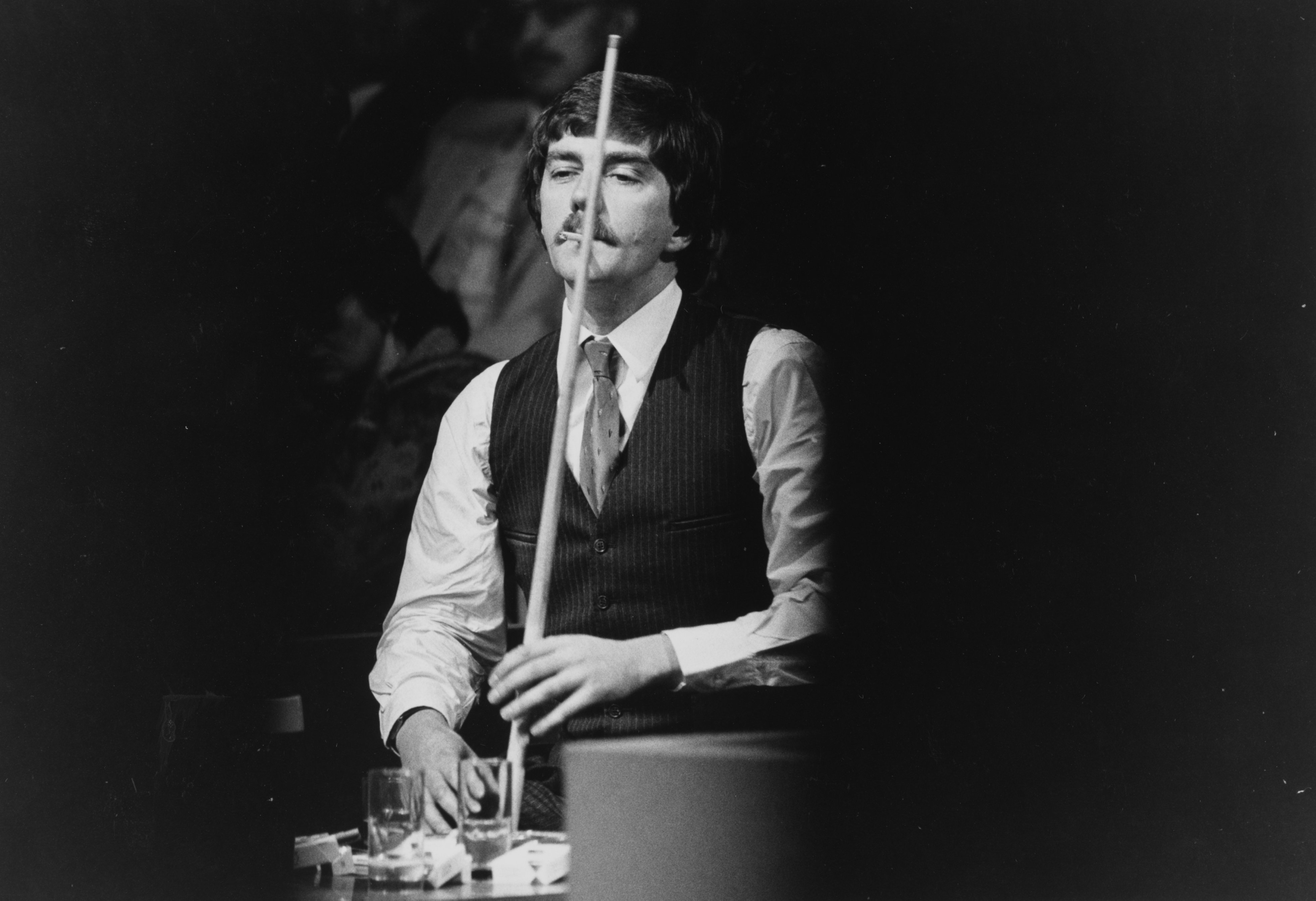 Black and white photo of Cliff Thorburn smoking during a snooker game.