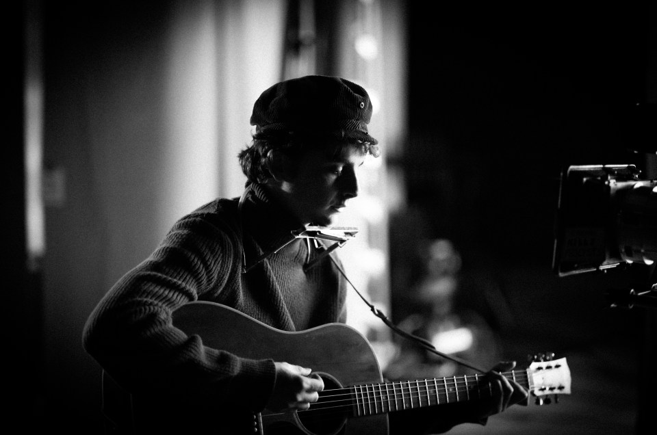 Black and white photo of Timothée Chalamet playing an acoustic guitar.