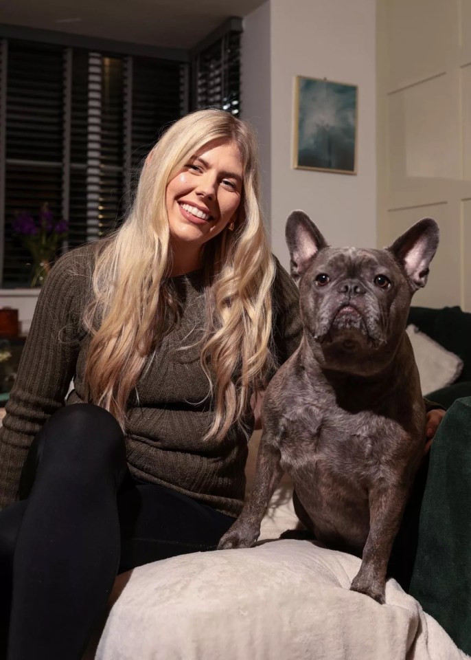 A woman sits on a couch with her large French bulldog.