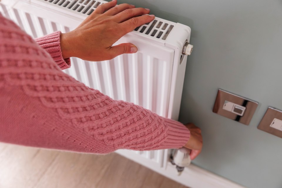 Woman's hands turning down the thermostat on a home radiator.