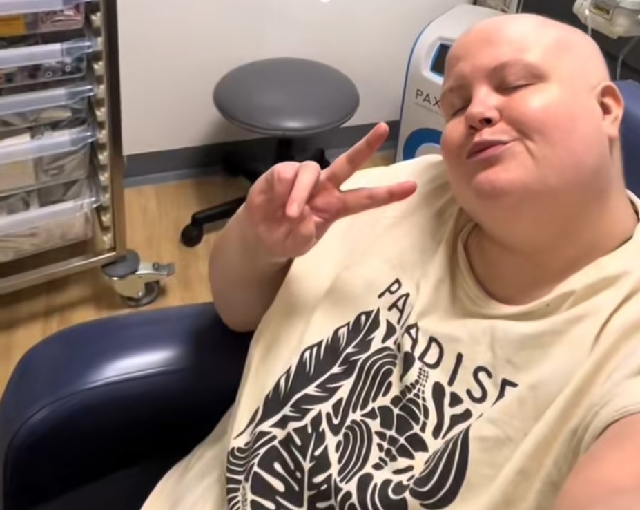 Woman with shaved head giving peace sign, during triple-negative breast cancer treatment.