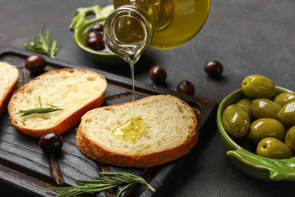 Olive oil being poured onto slices of bread with olives and rosemary.