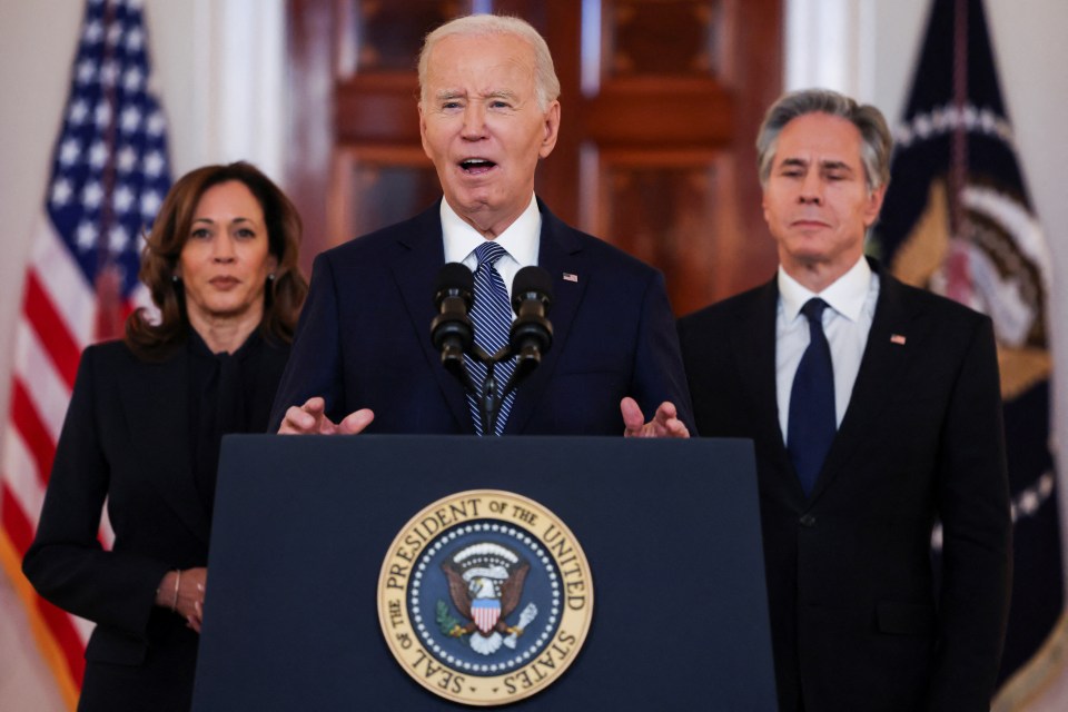 President Biden speaks at a podium flanked by Vice President Harris and Secretary of State Blinken.