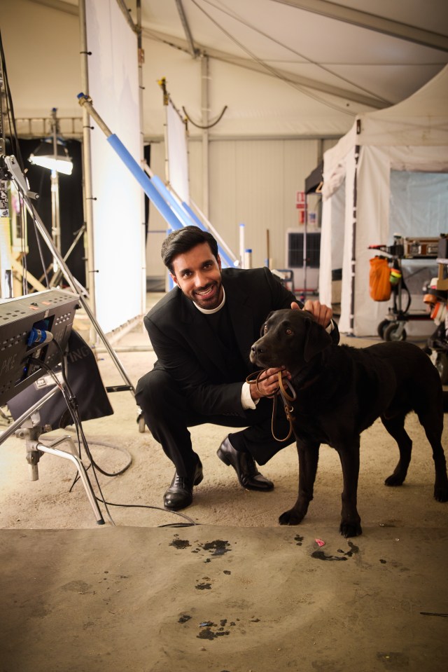 A man in clerical clothing crouching with a black Labrador.