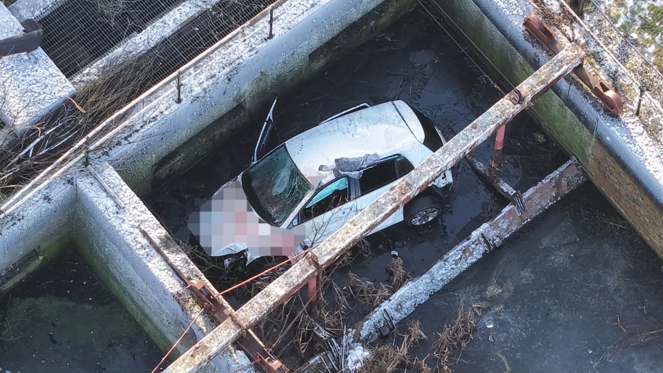 A wrecked car submerged in a sewage pit.