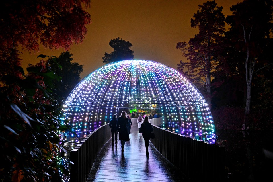 People walking across a bridge under a lighted dome at Kew Gardens.